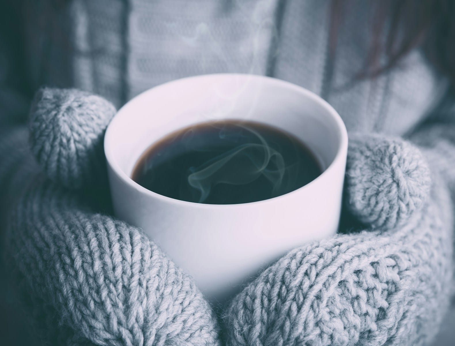Inclusive winter scene of gloved hands holding a ceramic mug of coffee